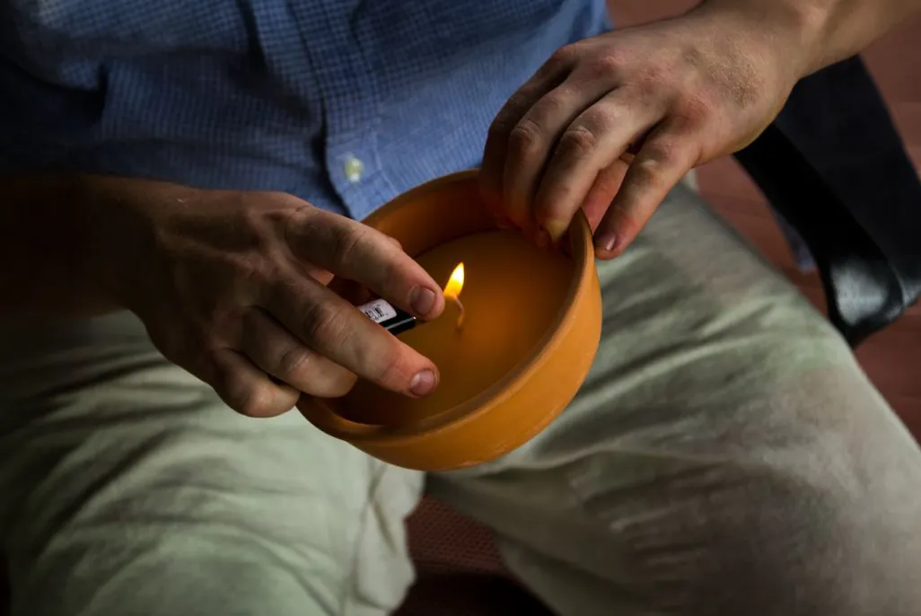 A person using a lighter to ignite a large citronella candle in a terracotta pot for outdoor mosquito control.