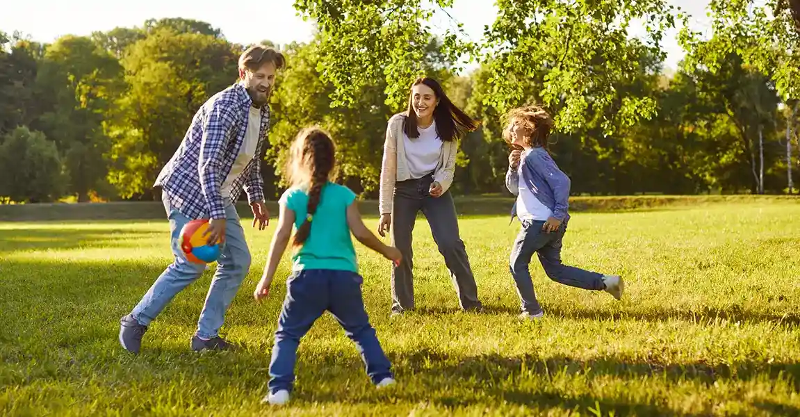 A family playing together with a colorful ball on a large, disease-free green lawn surrounded by healthy trees.