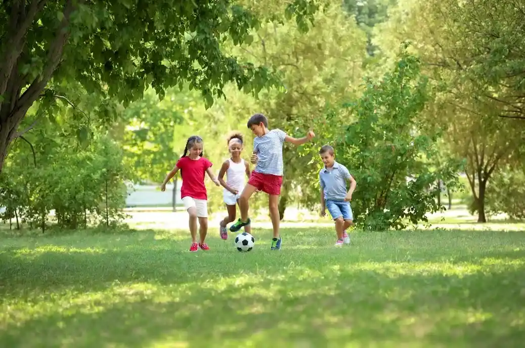 Four children safely playing soccer on the grass in a lush, green, mosquito-free backyard