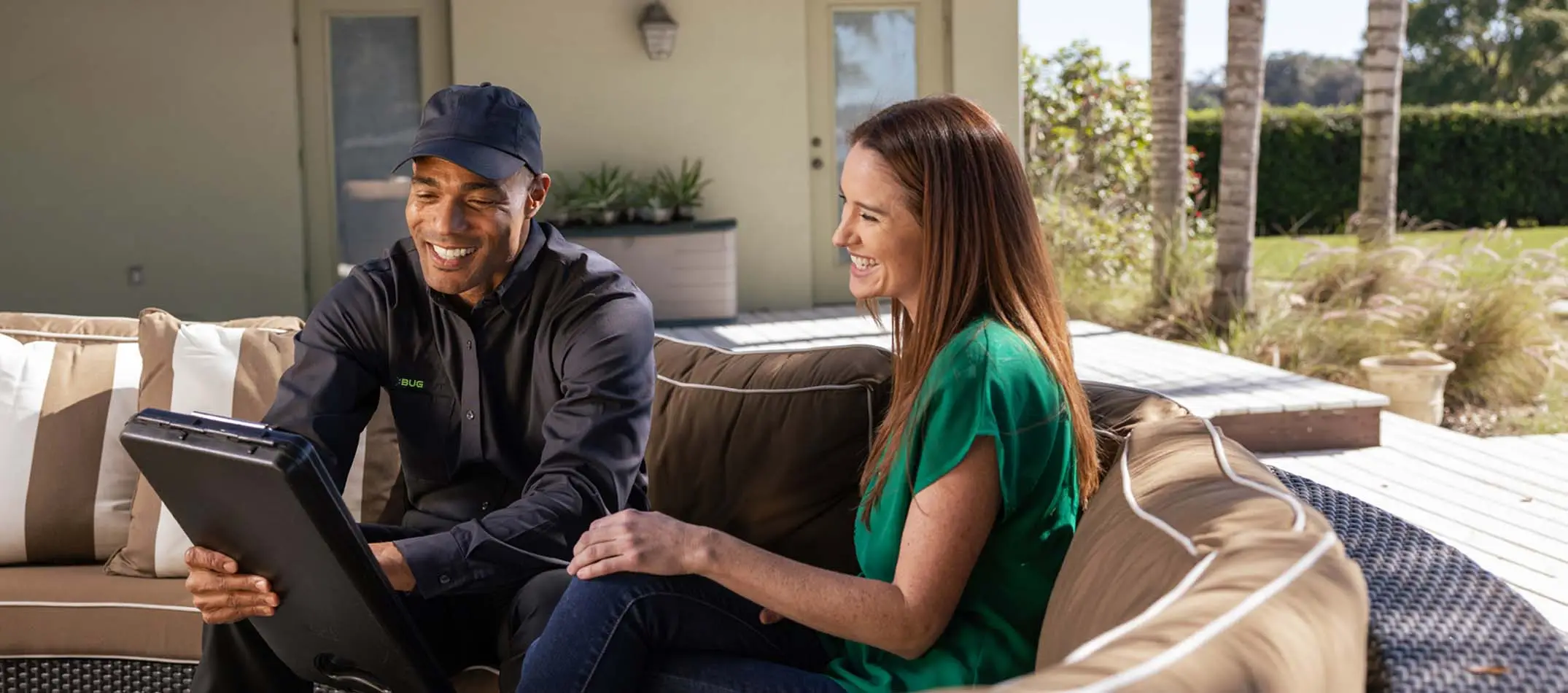 Technician sitting with a home owner on outdoor deck furniture talking and smiling