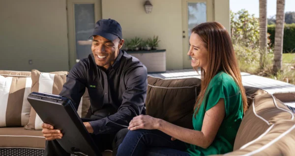 Technician sitting with a home owner on outdoor deck furniture talking and smiling